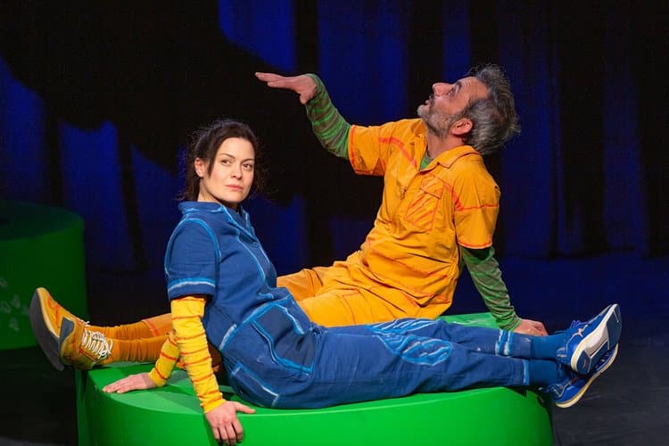 zwei Menschen sitzen sich gegenüber auf einem grünen Hocker, einer hält den Handrücken nach oben