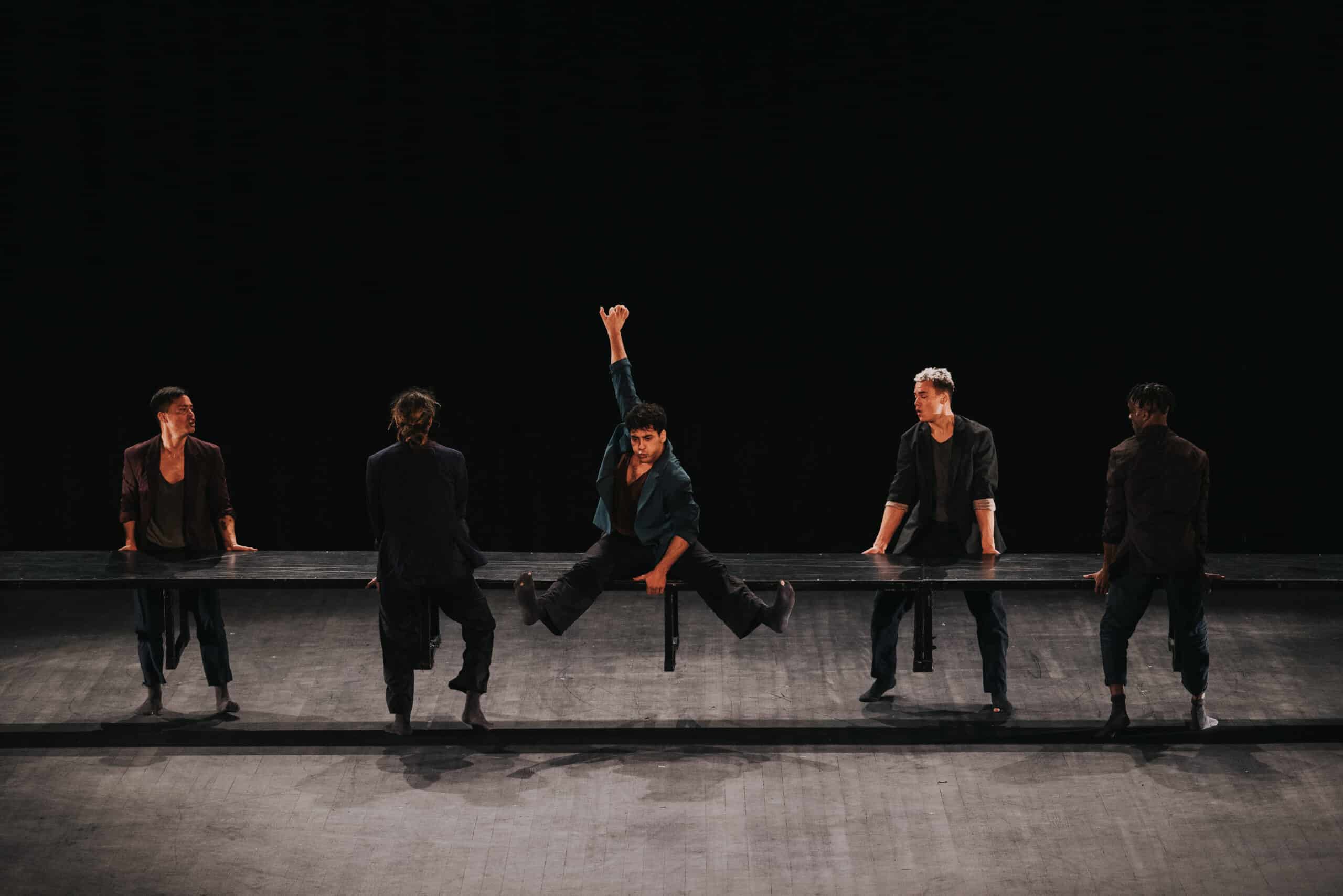 Tänzer heben eine schwarze Bank während einer darauf sitzt