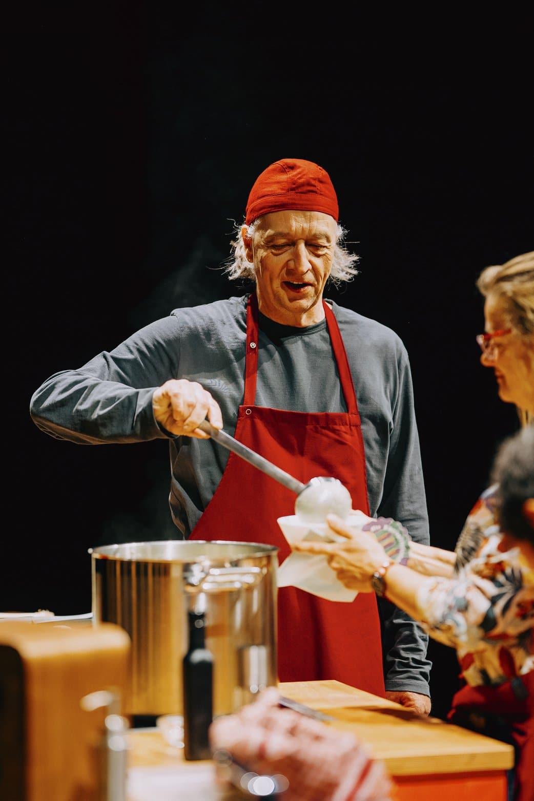Mann in Kochsachen, er teilt mit einer großen Kelle Suppe aus